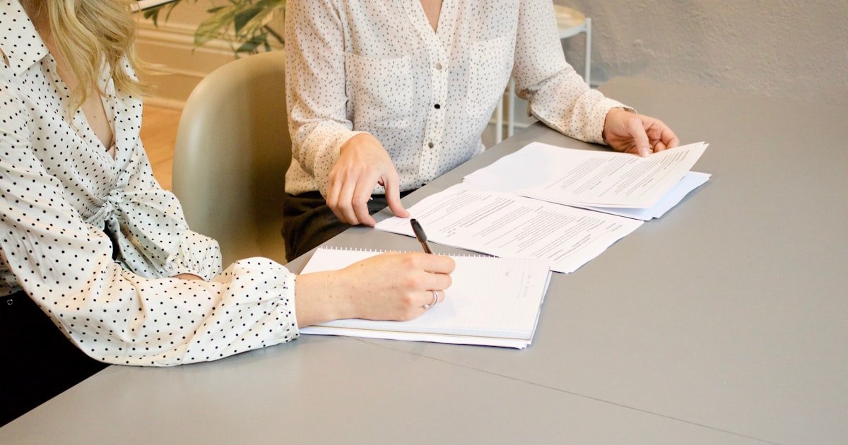 Duas pessoas assinando documentos sobre a mesa